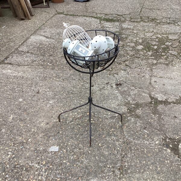 Vintage metal flower pot stand with lantern holders in a garden setting.