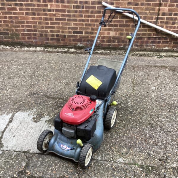 Side view of a used Honda petrol lawn mower in a garden setting.