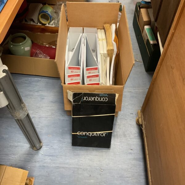Cardboard box filled with office supplies, including ring binders and envelopes.