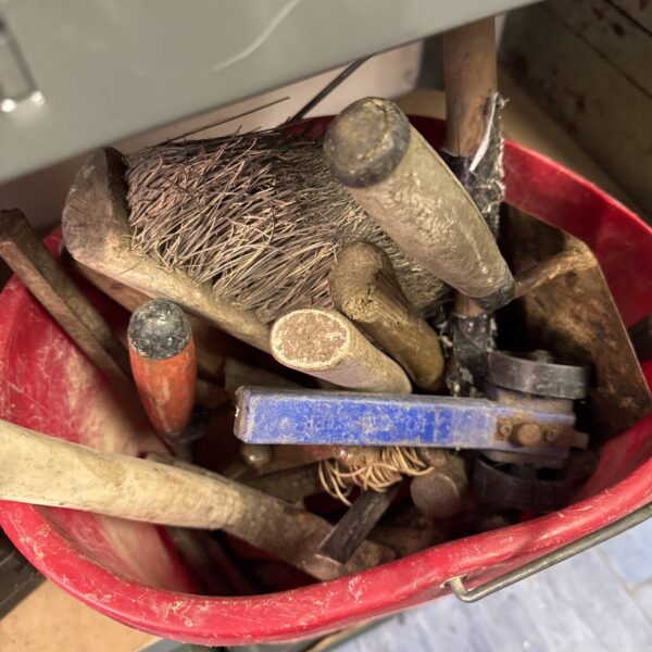 Vintage bricklayers tools including hammers and trowels in a bucket.