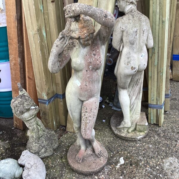 Vintage concrete garden statue of a nude lady in an outdoor setting.