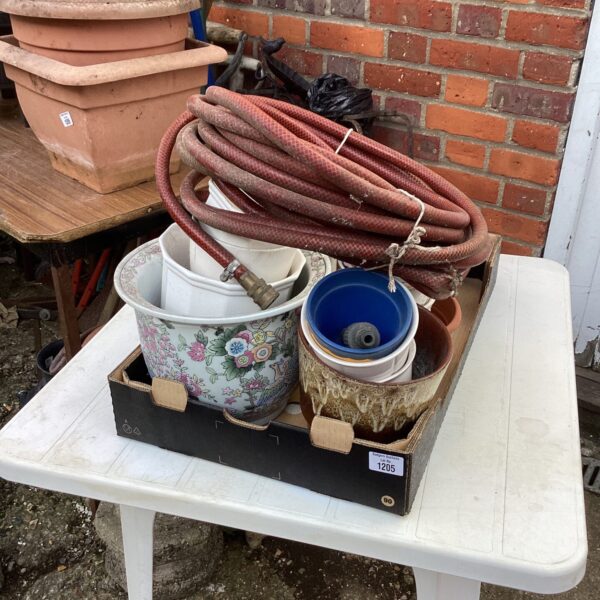 Collection of terracotta and floral garden pots with a coiled hose.