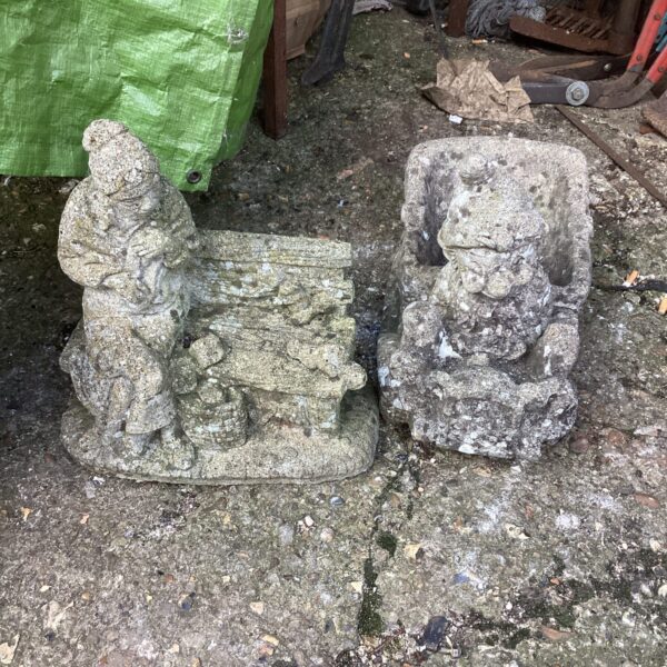 Weathered stone garden ornaments depicting figures in a garden setting.
