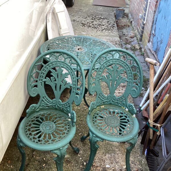 Vintage metal patio set with floral detailing in a garden setting.