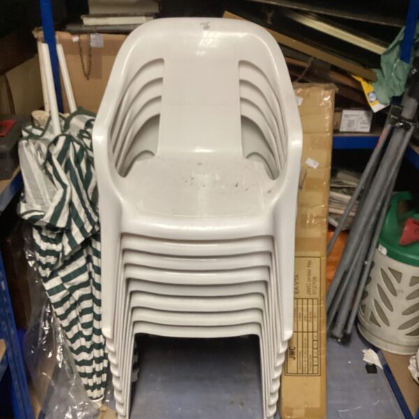 Lot of eight white plastic patio chairs stacked for storage.