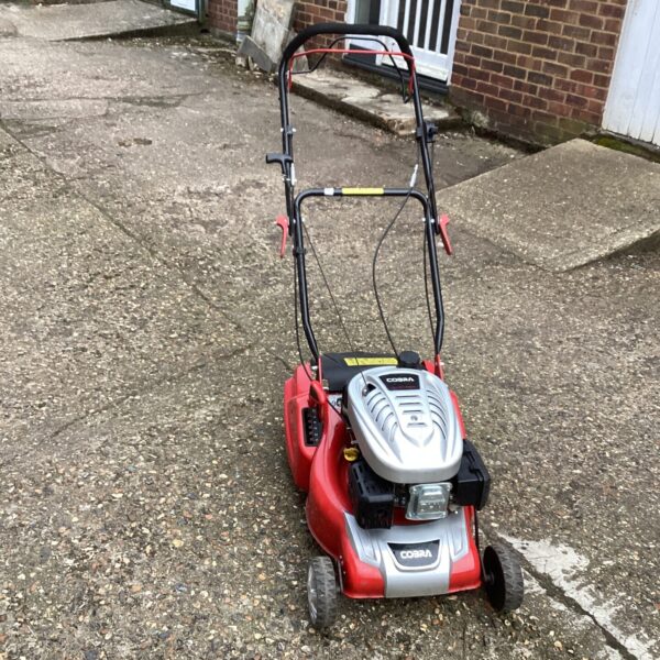 Red and black Cobra petrol lawn mower in a garden setting.