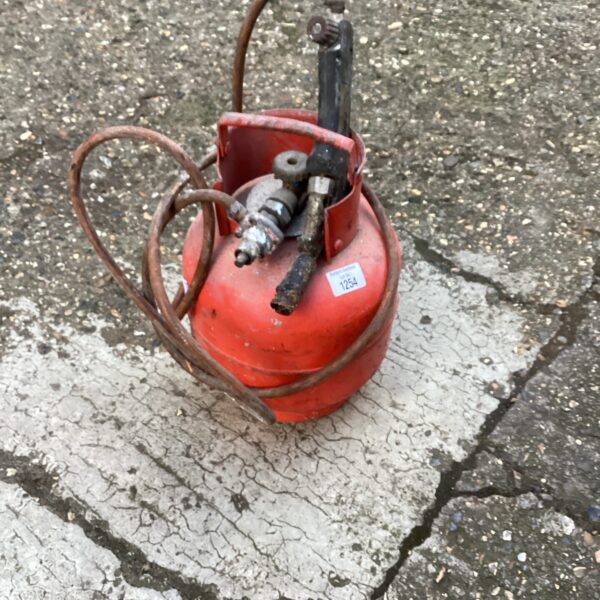 Vintage red gas bottle with attached torch for industrial use.