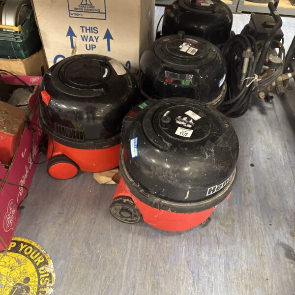 Three red Numatic Henry Hoover bodies stacked for spares or repair.