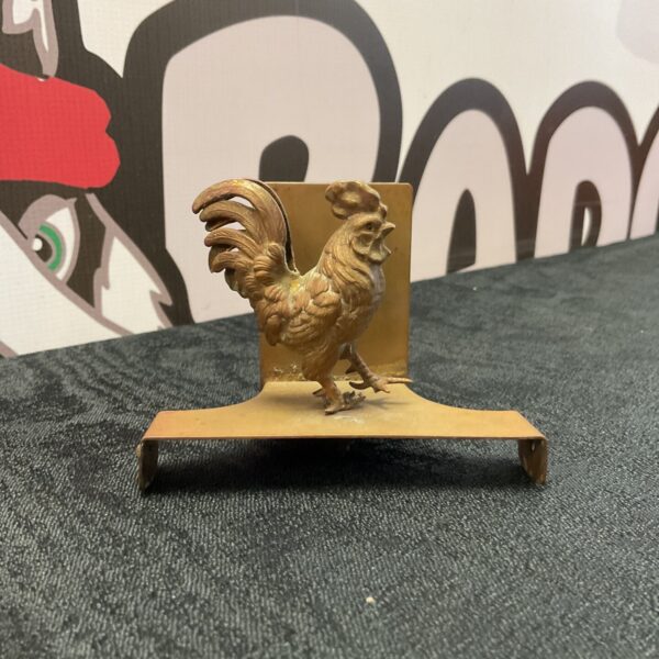 Vintage copper cockerel match holder on a dark surface.