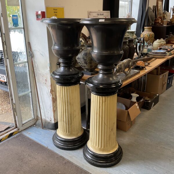 Black marble effect urns on black columns, decorative garden display.