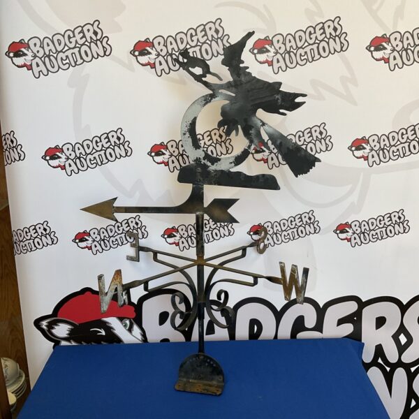 Vintage metal witch weather vane in a garden setting.