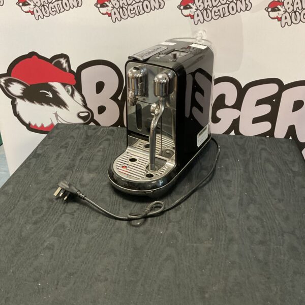 Front view of a silver Sage Nespresso coffee machine on a grey surface.