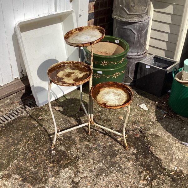 Vintage metal plant pot stand with tiered shelves in a garden setting.