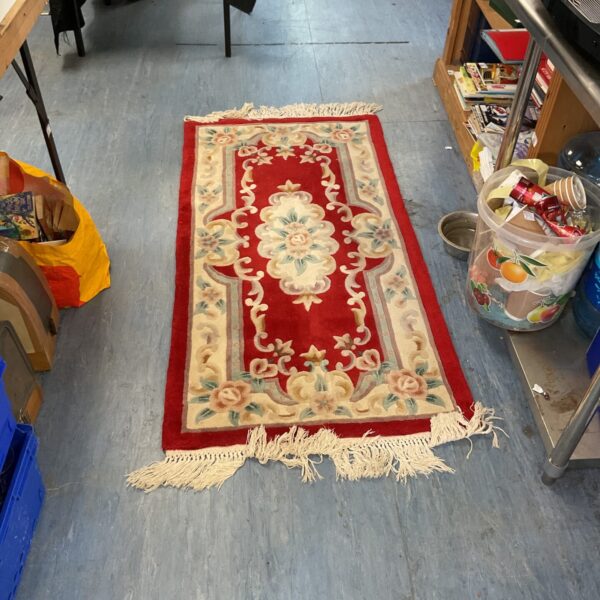 Red floral runner rug with fringed edges, vintage style.