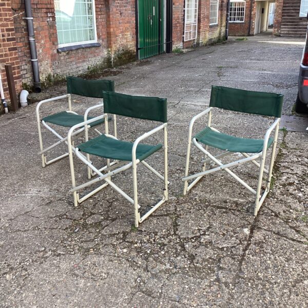 Three vintage folding canvas chairs in a garden setting.