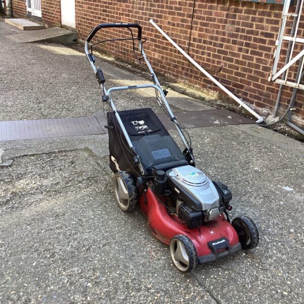 Side view of a used Einhell petrol lawn mower in a garden setting.