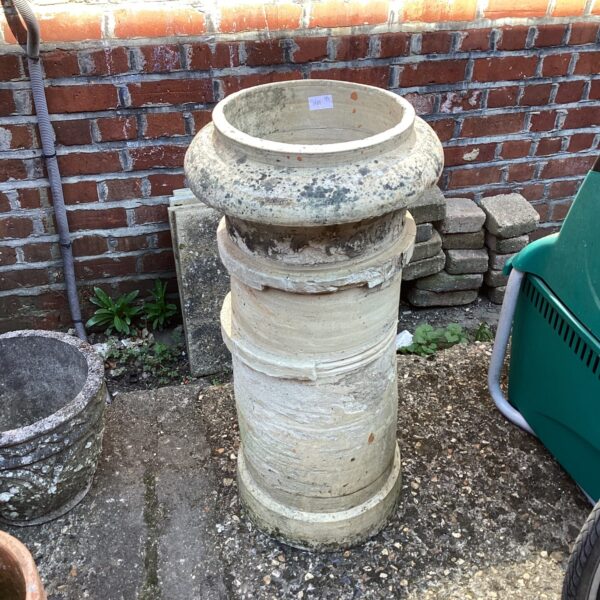 Tall terracotta chimney pot in a garden setting.