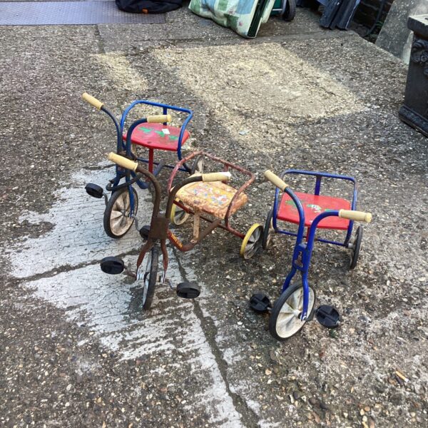 Lot of three vintage child's tricycles in a garden setting.