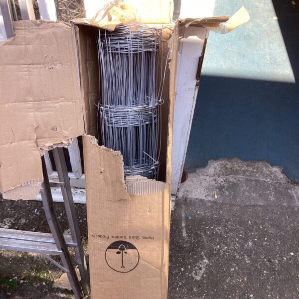 Partially dismantled cardboard packaging containing a roll of wire fencing.