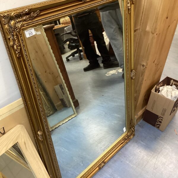 Large gold framed mirror with ornate detailing.