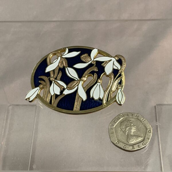 Vintage Monet enamel snowdrop brooch on a tiled surface.