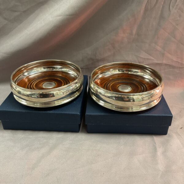 Pair of antique silver wine bottle coasters on a navy background.