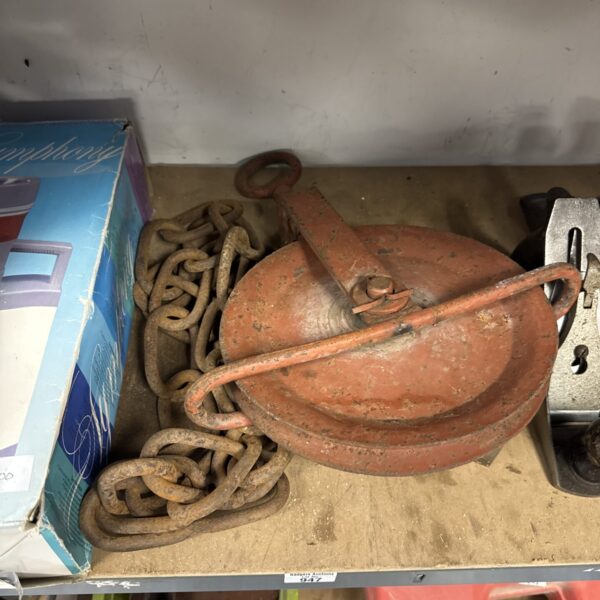 Vintage metal pulley wheel with attached chain for antique restoration.