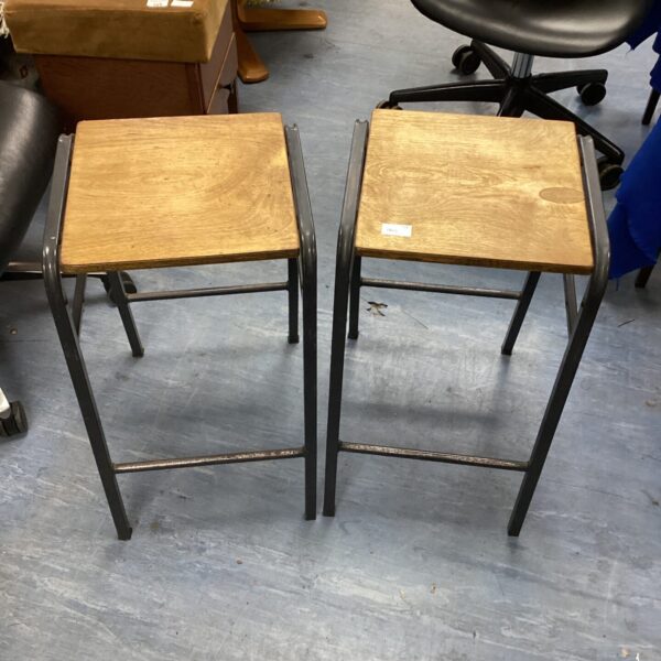 Two vintage wooden stools with metal frames for seating.