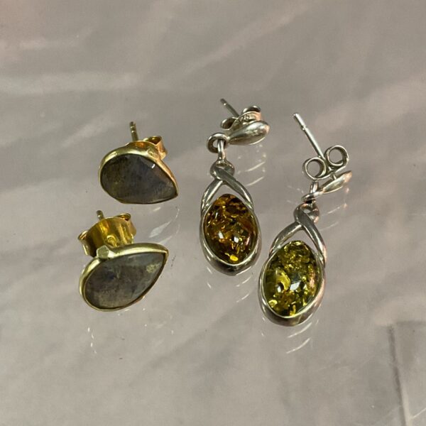 Close-up of two pairs of silver stud earrings with gemstones.