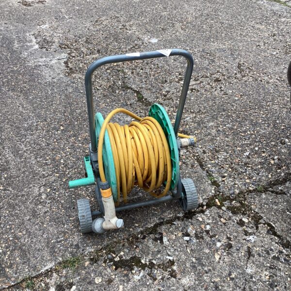 Vintage garden hose reel with yellow plastic hose in outdoor setting.