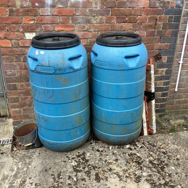 Two weathered plastic water butts in a garden setting.