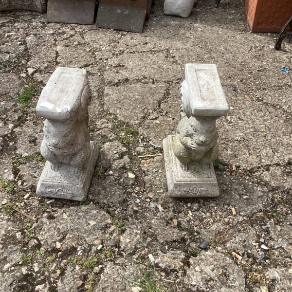 Weathered stone squirrel bench ends in a garden setting.