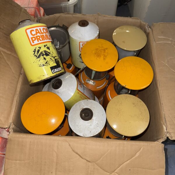 Vintage Primus camping lanterns and gas canisters in a cardboard box.