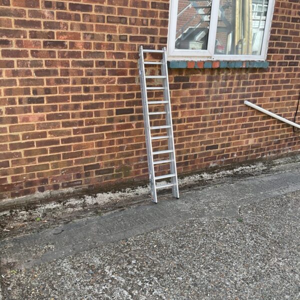 Silver aluminium loft ladder folded against a brick wall.