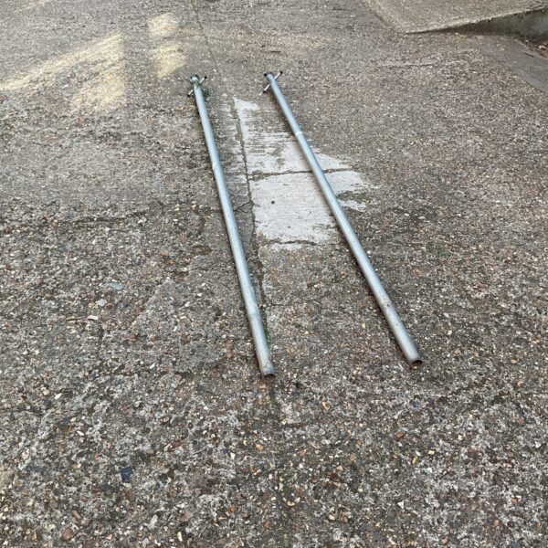 Two weathered metal clothes line poles in a garden setting.