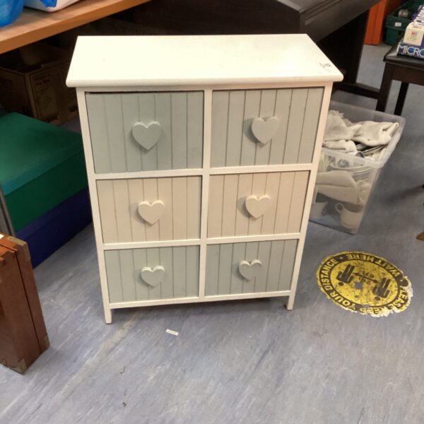 Pale grey bedroom drawers with heart-shaped handles for storage.
