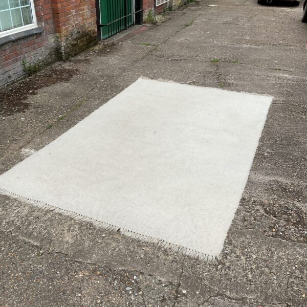 Large white wool rug displayed outdoors on a paved surface.