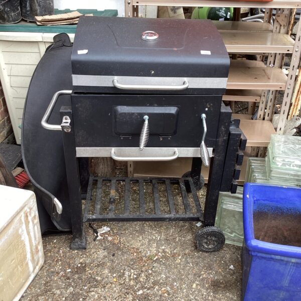 Black metal BBQ grill in a garden setting.