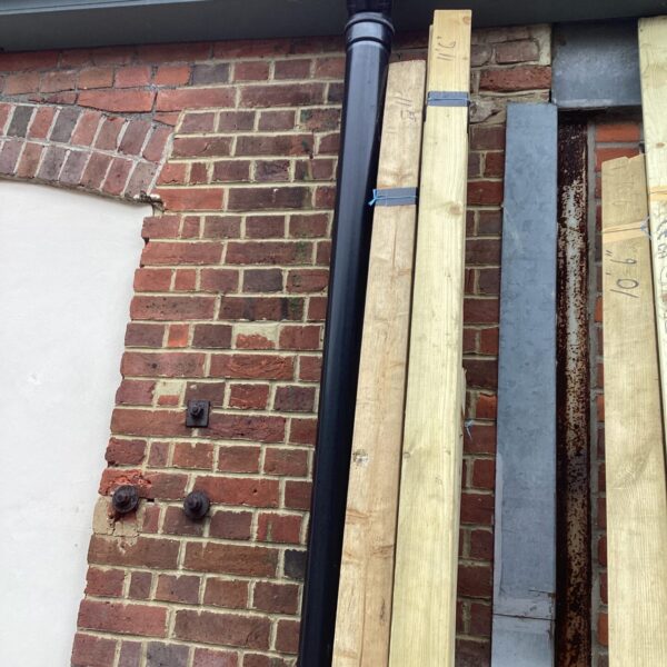 Exterior view of three bundles of timber leaning against a brick wall.