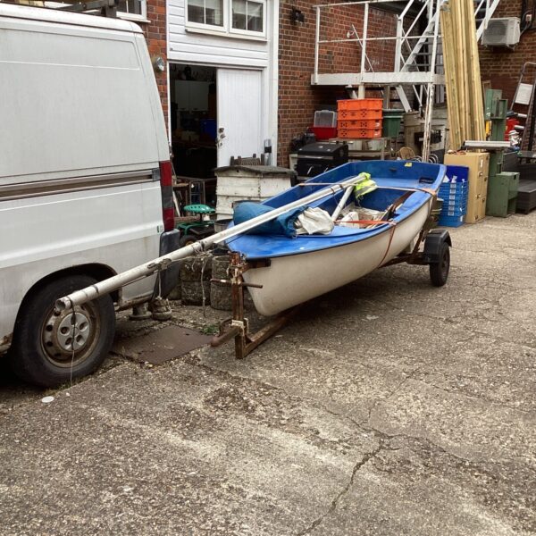 White and blue sailing dinghy on a trailer, ready for restoration.