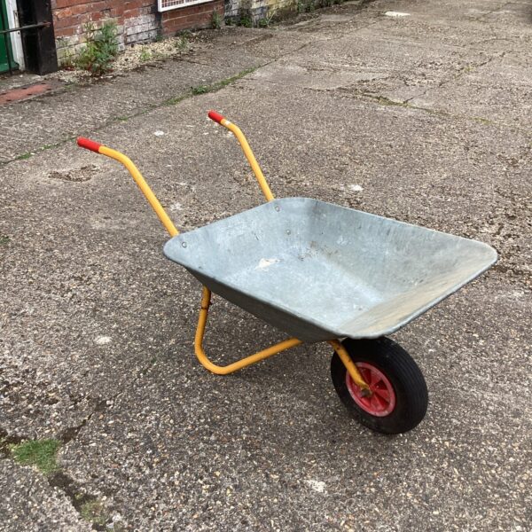 Vintage galvanised wheelbarrow in a garden setting.