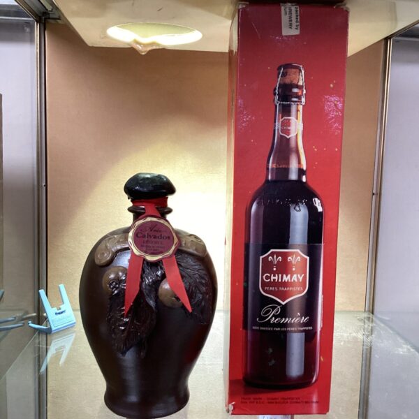 Front view of a sealed Chimay bottle with a stoneware jug.