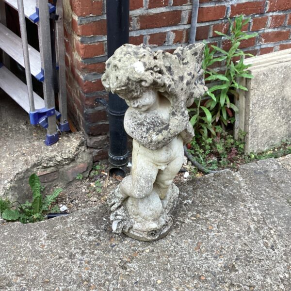 Weathered stone cherub garden ornament in a garden setting.
