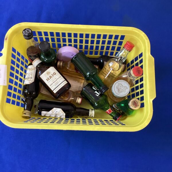 Assorted miniature spirit bottles in a yellow basket, collectible display.