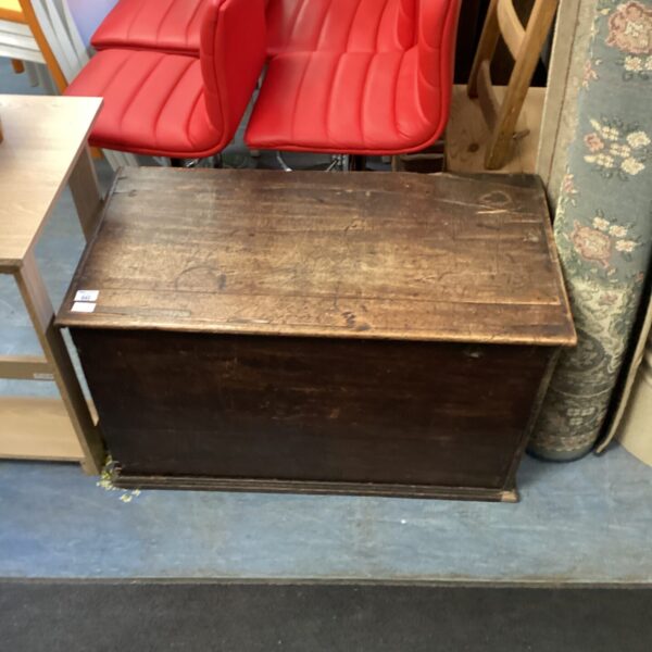 Antique 19th-century wooden chest with red chairs in background.