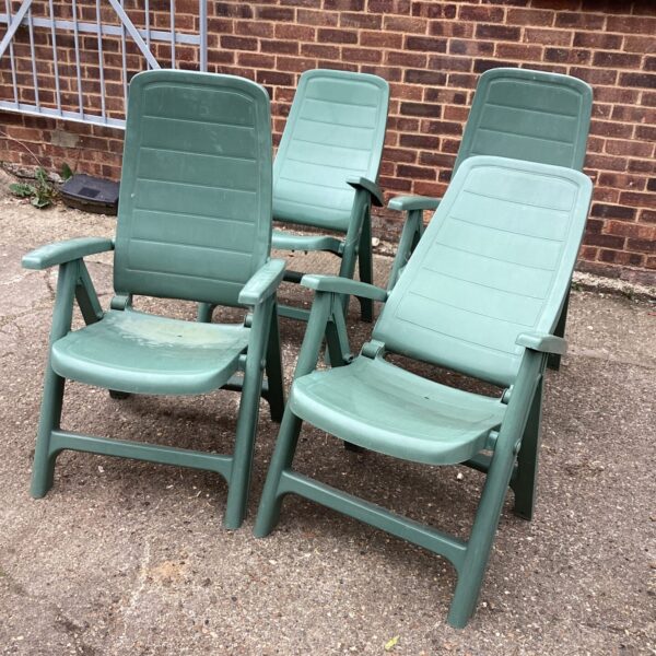 Four plastic recliner garden chairs in a garden setting.