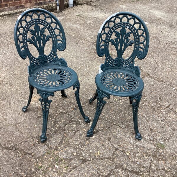 Pair of antique metal garden chairs with ornate detailing.