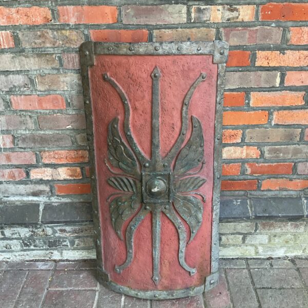 Red fibreglass Roman shield replica against a brick wall.