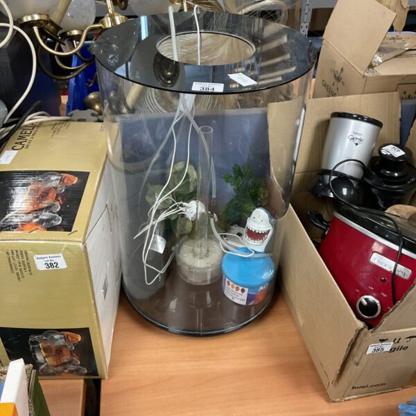 Circular fish tank with gravel, plant, and fish food displayed.