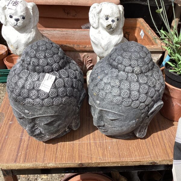 Two weathered stone Buddha heads in a garden setting.